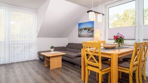 Un salon moderne comprenant un canapé, une table à manger avec des chaises, une petite table d’appoint et un luminaire suspendu.
