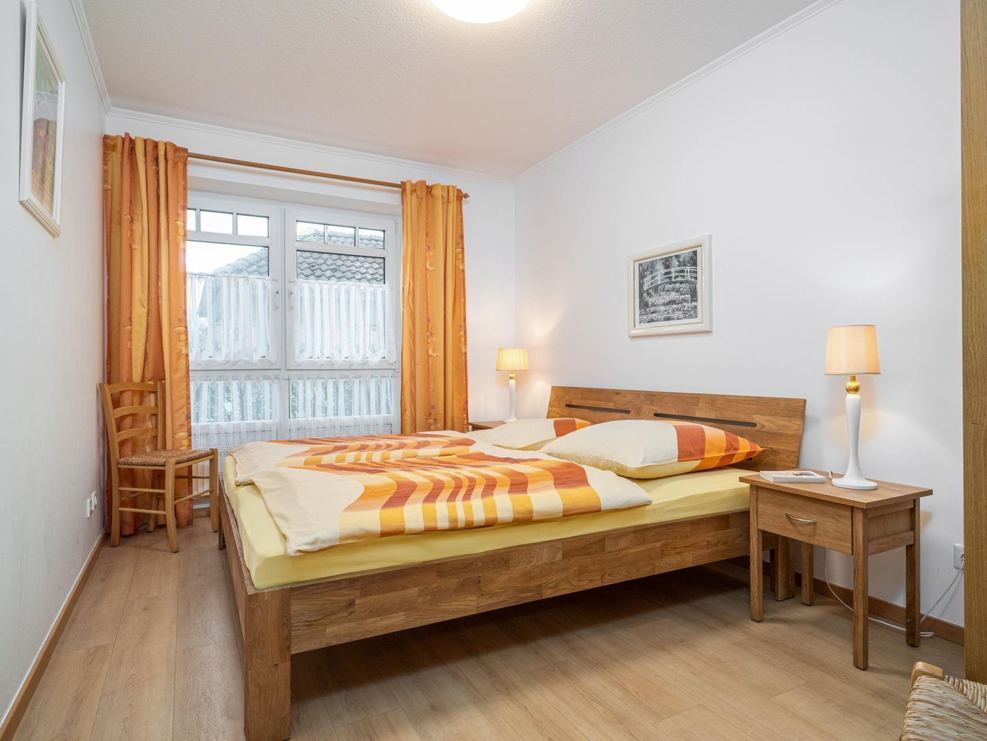 Ein Schlafzimmer mit einem hölzernen Bett, zwei Nachttischen, einem Sessel und einem Fenster mit Vorhängen.