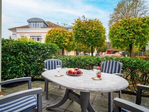 An outdoor patio with a round table and chairs, surrounded by greenery and trees. - Villa Nicole - Apartment 01 - Comfortable vacation apartment in Zingst with terrace and (Zingst (Ostseeheilbad))