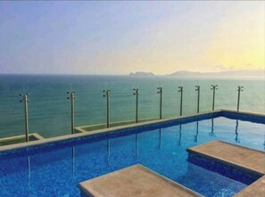 An infinity pool with a view of the sea and distant land. - Panoramic San Miguel Apartment (Lima)