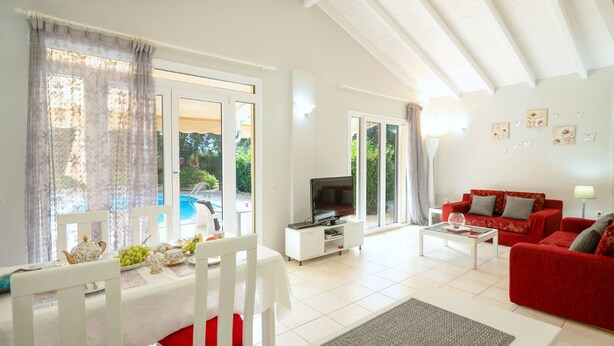 A spacious living room with a red sofa, a white coffee table, and a dining area with a table set for two. - Relax near Corfu’s finest beaches in this charming villa for up to 4 guests (Halikounas)