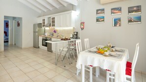 A modern kitchen with white cabinets, a dining area with a table set for four, and a hallway leading to another room. - Relax near Corfu’s finest beaches in this charming villa for up to 4 guests (Halikounas)