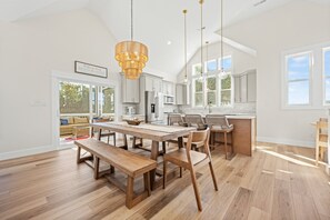 A spacious kitchen with a large wooden table and chairs, white cabinets, and a hanging light fixture. - Bubbles Up: Private Pool, Hot Tub, Currituck Club Resort (Corolla)
