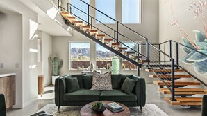 Ein geräumiges Wohnzimmer mit einem grünen Sofa, einem Couchtisch und einer Treppe mit Holzstufen und Metallgeländern.