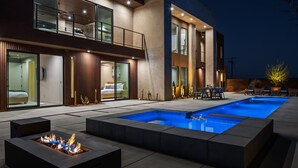 Ein modernes, zweistöckiges Haus mit Swimmingpool, Sitzgelegenheiten im Freien und einem Feuerkorb.