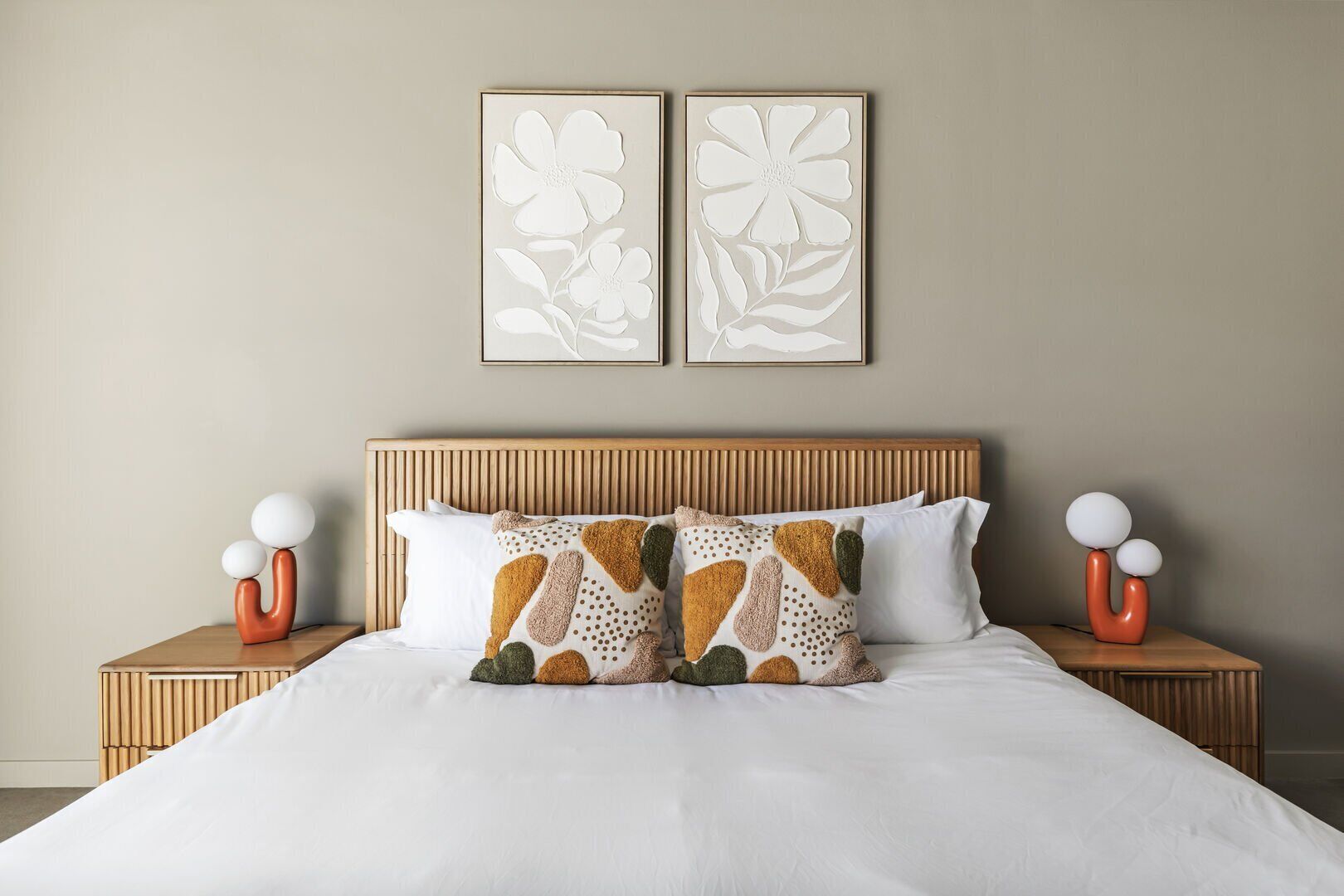 A neatly made bed with white bedding, two pillows with geometric patterns, and two wall-mounted picture frames with floral designs.