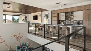 Eine moderne Küche mit Holzschränken, ein Essbereich mit einem hohen Tisch und Stühlen sowie eine Treppe mit Geländer.