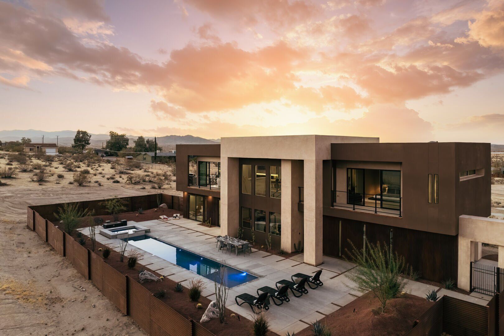 A modern two-story house with a swimming pool, outdoor seating, and a desert landscape in the background.