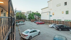 Un aparcament amb diversos cotxes, un edifici blanc amb finestres i una tanca.