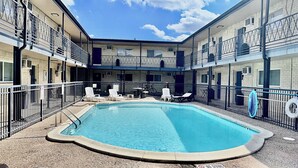 Una piscina amb gandules i un senyal de prohibició de salts, envoltada per un pati tancat amb un edifici de maó.