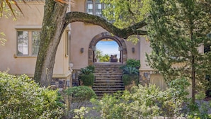 Un bâtiment doté d’un escalier en pierre menant à une entrée abritée, le tout entouré d’une végétation luxuriante.