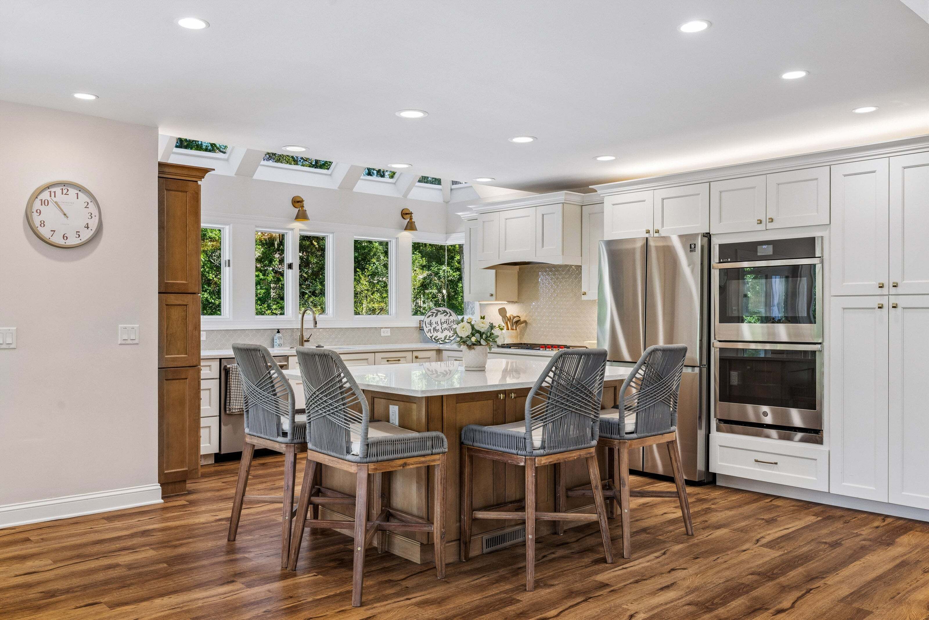 A modern kitchen with a central island, white cabinetry, stainless steel appliances, and a wooden floor.