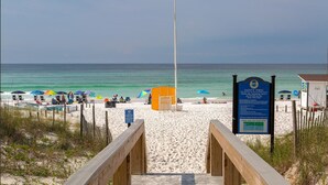A beach with a wooden walkway leading to the water, beach umbrellas, and a lifeguard stand.