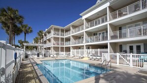 A hotel with a swimming pool, multiple balconies, and palm trees.