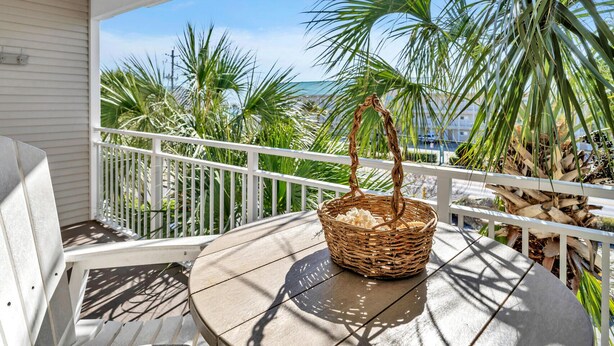 A covered outdoor seating area with a wicker basket on a table, surrounded by palm trees and a white railing.