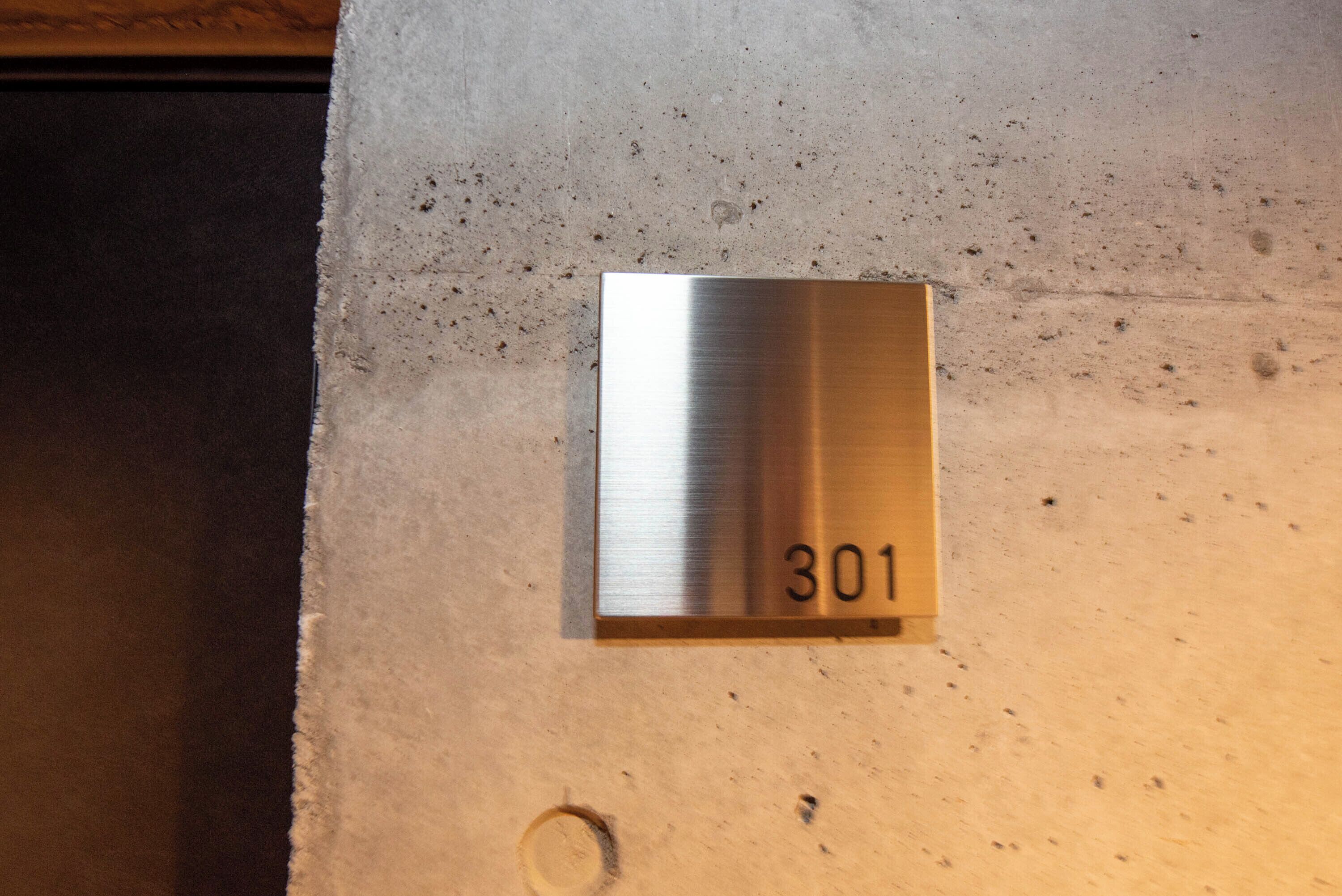 A metallic room number plaque with the number 301 on a textured wall.