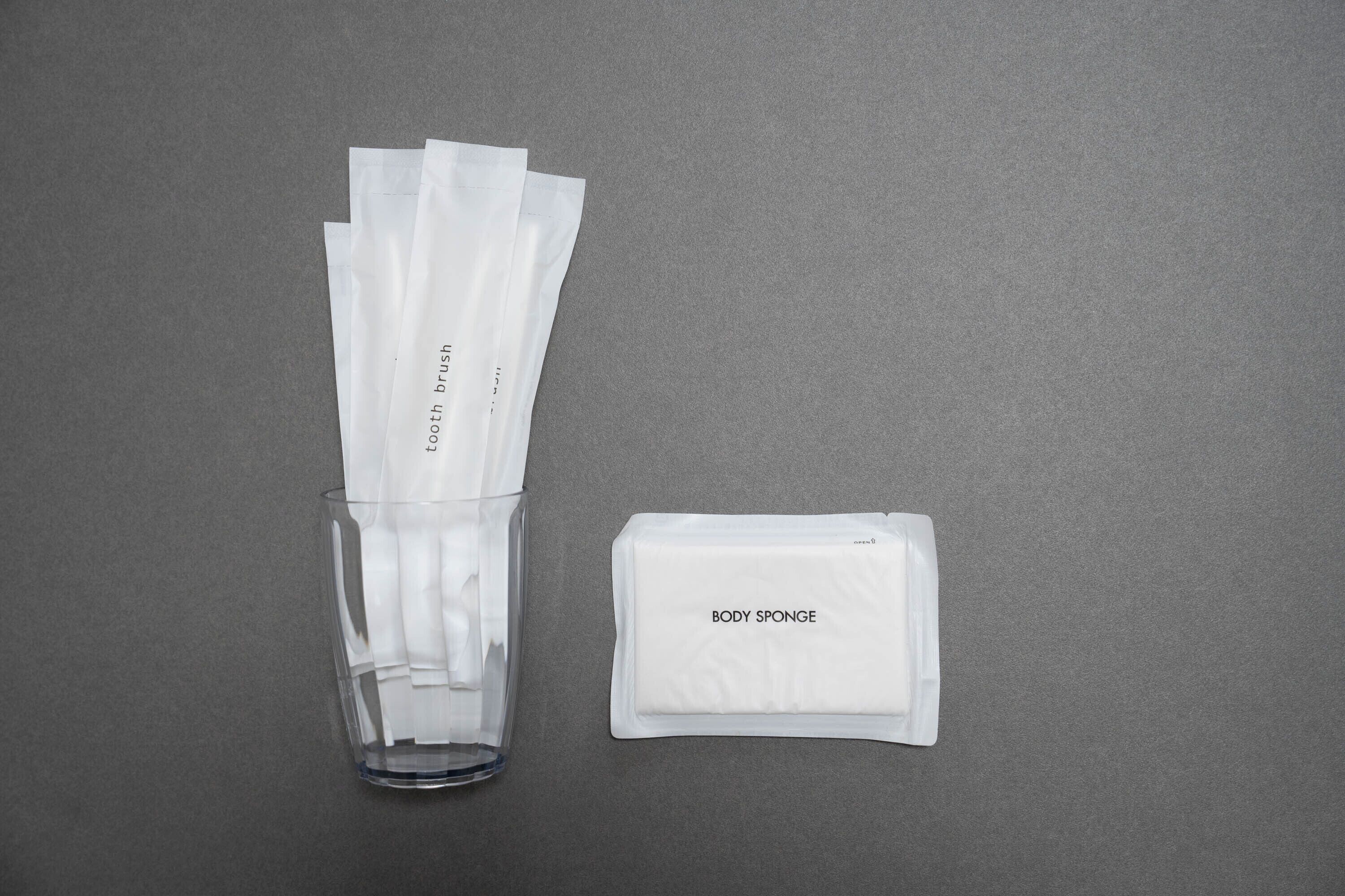 Ein durchsichtiges Glasgefäß mit weißen Handtuchrollen und einer weißen Packung mit der Aufschrift „BODY SPONGE“.