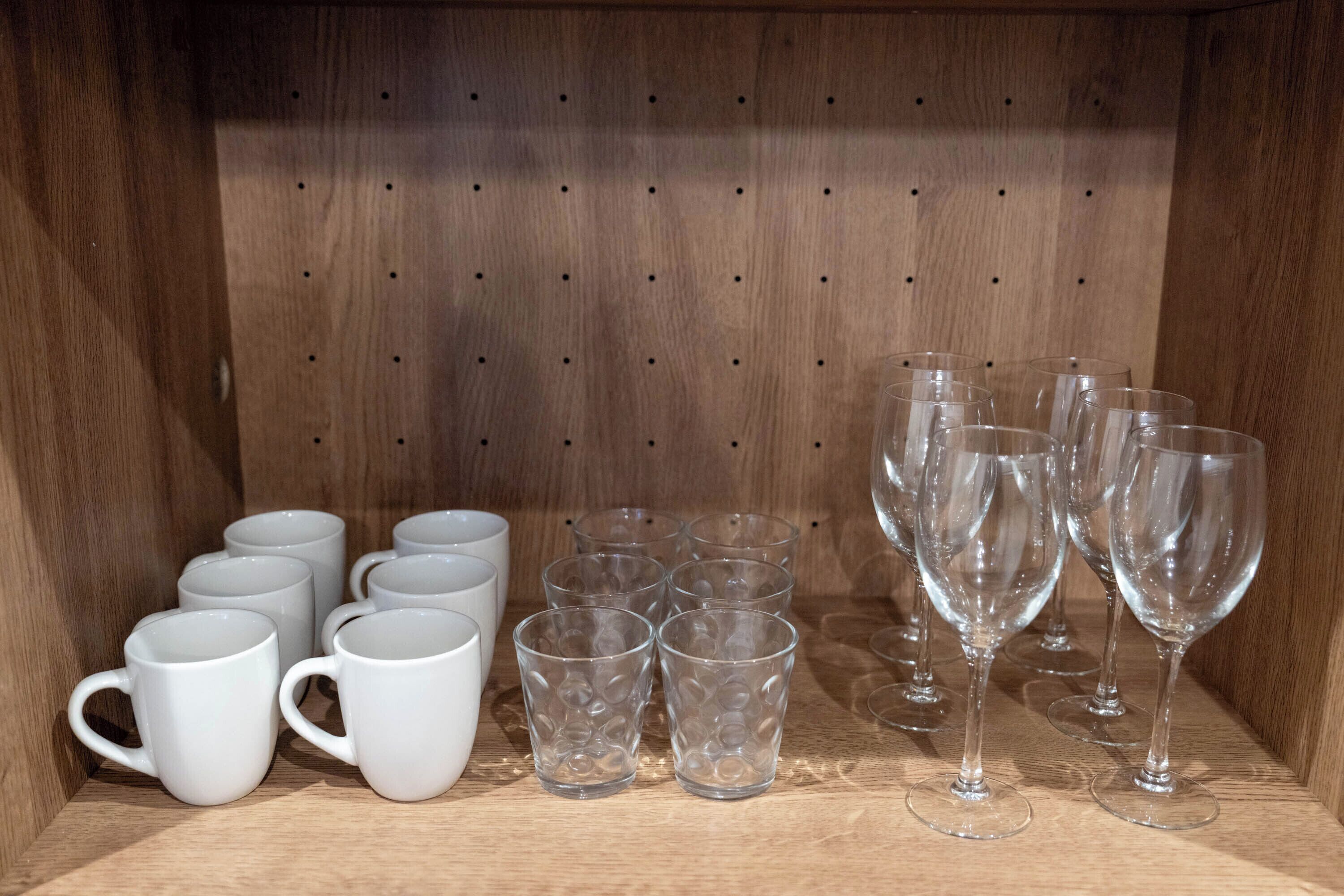 A wooden shelf with various glassware, including white mugs and clear glasses.