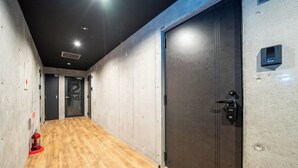 A hallway with a wooden floor, a fire extinguisher, and a door with a security lock. - ZABO HILLS 301 (Sapporo)