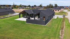 Une maison moderne aux murs noirs, dotée d’un patio abrité et d’une grande fenêtre.