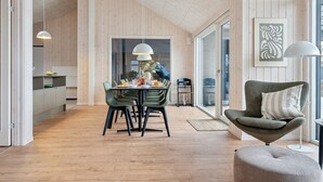 Un intérieur moderne avec un plancher en bois, un coin repas avec des chaises vertes, un canapé gris et une grande fenêtre.