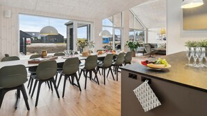 Un espace repas moderne avec une longue table, des chaises et un saladier rempli de fruits.