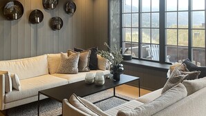 A cozy living room with a beige sofa, a coffee table, and a view of a rural landscape through large windows.