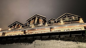 A multi-story hotel with a stone facade, wooden balconies, and a snow-covered ground.