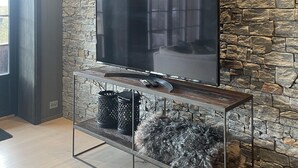 A modern living room with a stone wall, a flat-screen TV mounted on a wooden console table, and a fluffy rug on the floor.