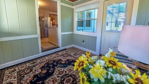 A room with a patterned rug, a door leading to a kitchen, and a window with blinds. - Family Stays: Middletown, CT (Middletown)