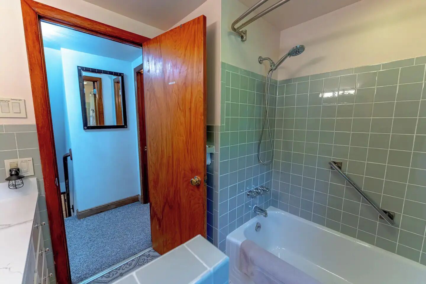 Un bany amb banyera, dutxa i una porta de fusta que dona a una altra habitació.