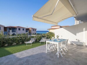A patio with a table and chairs, a white umbrella, and a view of the sea.