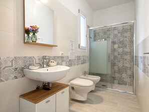 A bathroom with a large sink, two toilets, a shower enclosure, and patterned tiles.