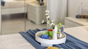 Una bandeja ordenada con una taza, un pequeño florero con flores y un salero y pimentero sobre una cama con una toalla azul.