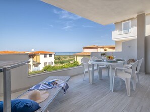 Un balcón con una mesa y sillas, una banca, y vistas al mar y edificios cercanos.