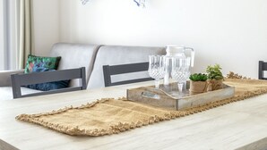 Un comedor con una mesa de madera, dos sillas, un posavasos tejido, una jarra de vidrio y dos vasos.