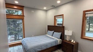 A bedroom with a bed, nightstands, and a window with a view of trees. - Riverview Retreat! Near Trails! (Fort Kent)