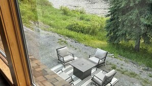 A patio with a table and chairs overlooking a river and forested area. - Riverview Retreat! Near Trails! (Fort Kent)