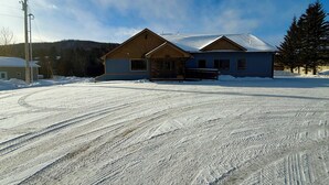 A two-story house with a snow-covered driveway and a wooden porch. - Riverview Retreat! Near Trails! (Fort Kent)