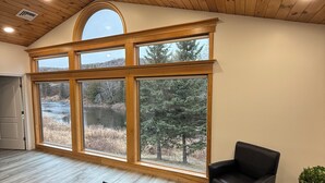 A spacious room with large windows, a wooden ceiling, and a patterned rug. - Riverview Retreat! Near Trails! (Fort Kent)