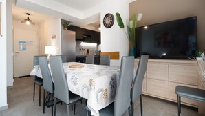 A modern dining area with a table set for four, a television on the wall, and a kitchen in the background. - Bright villa 8 ppl, garden, close to the sea (Sérignan)