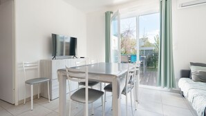 Una habitación moderna con una mesa de comedor, sillas, televisión y un balcón con cortinas.