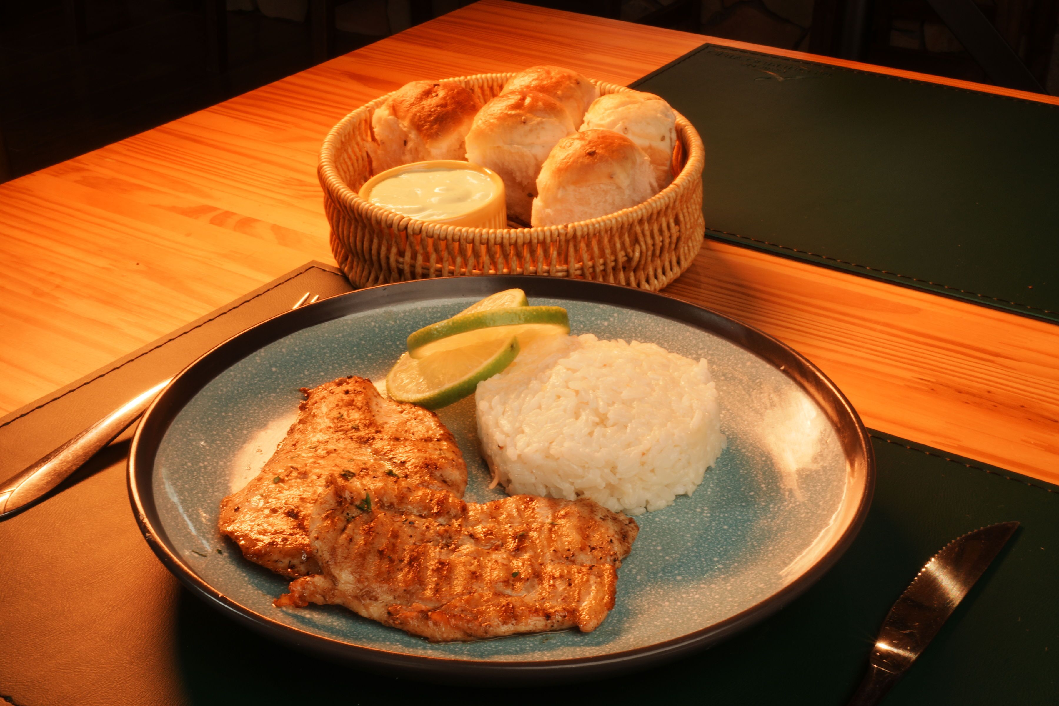 Un plato con pescado a la parrilla, arroz y una guarnición de pan y mantequilla.