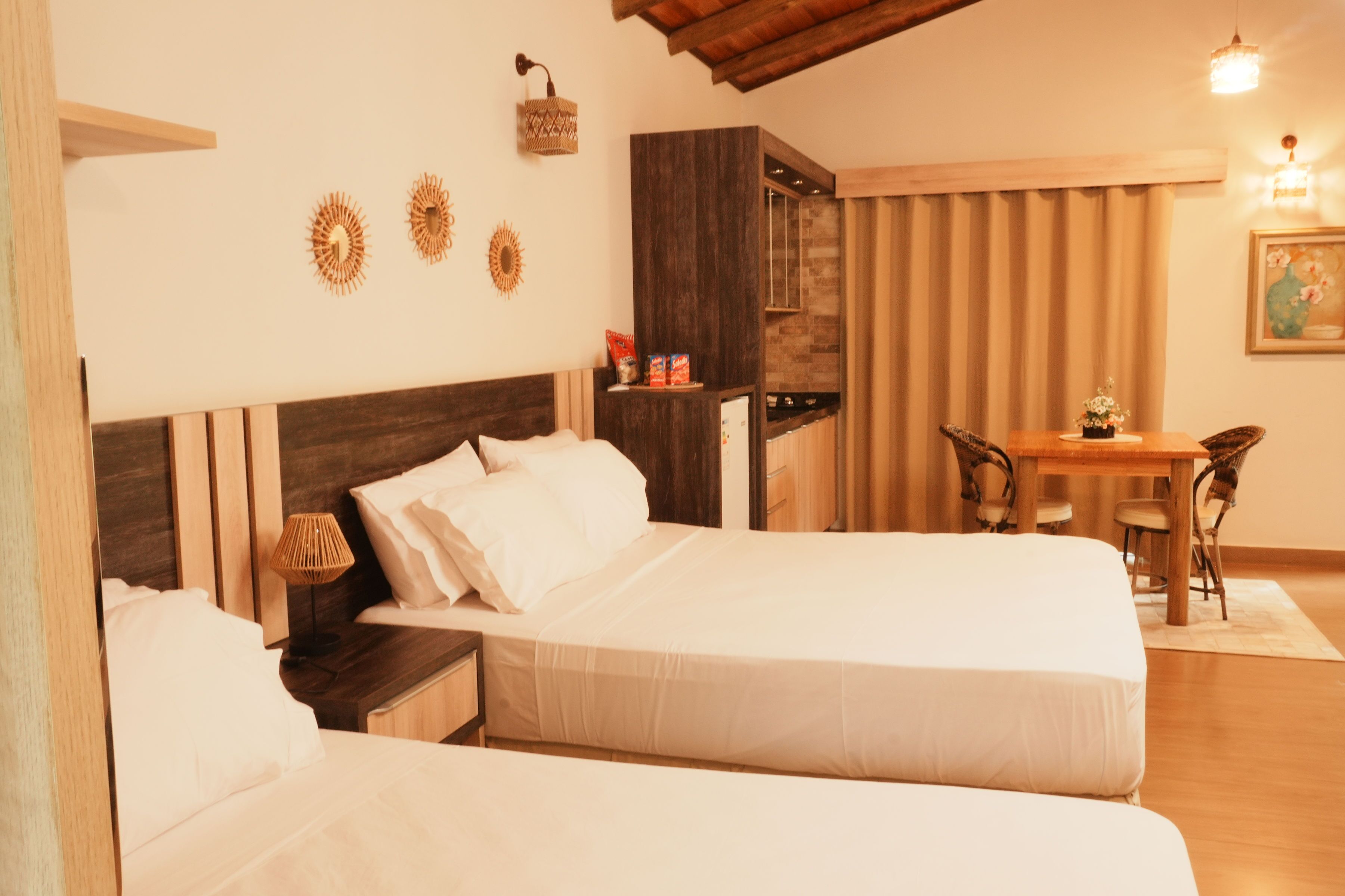 Une chambre d’hôtel avec deux lits, une tête de lit en bois, une petite table avec des chaises et une étagère murale agrémentée d’objets décoratifs.