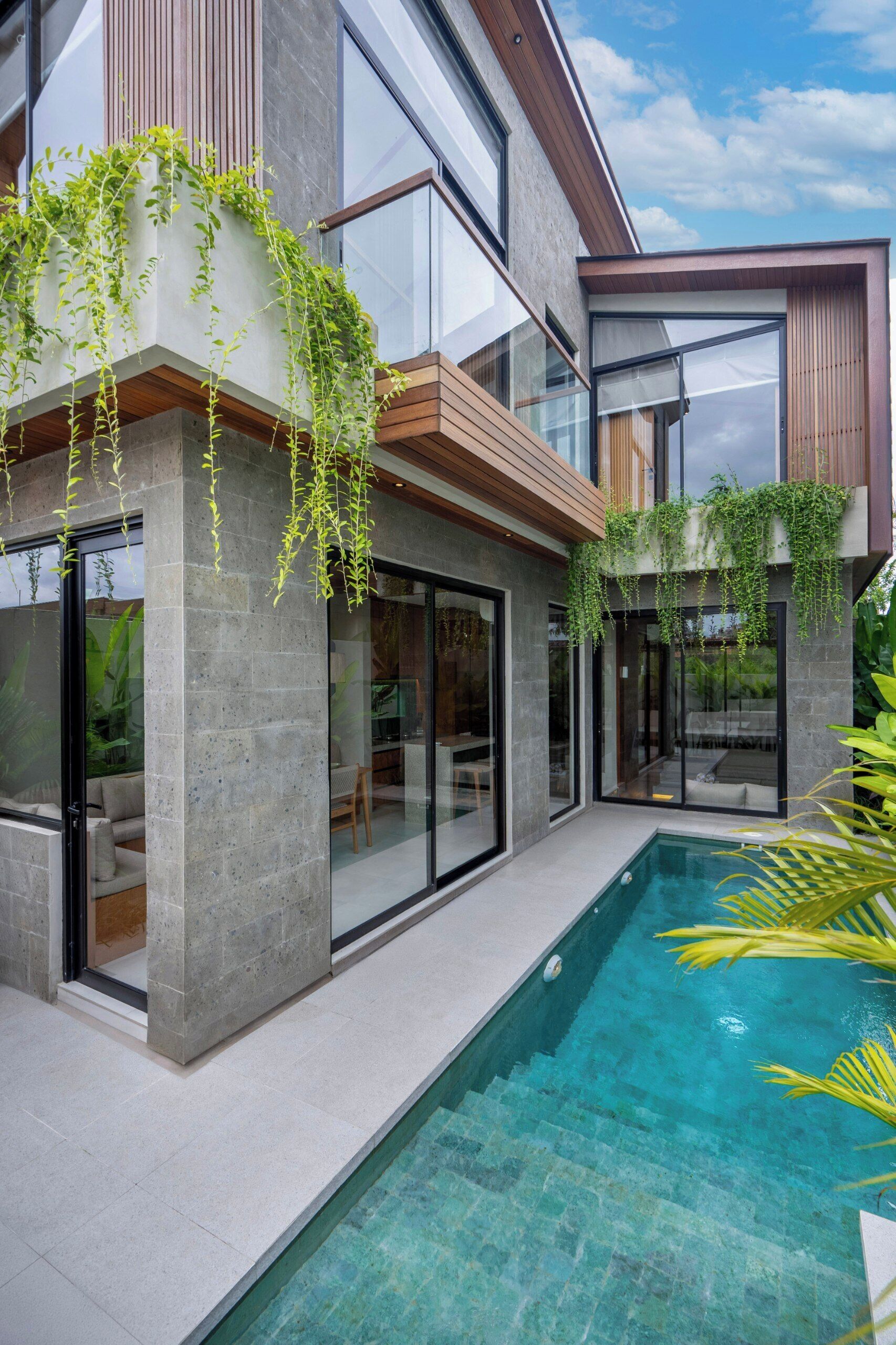Ein modernes Haus mit Swimmingpool, großen Glasfenstern und einem Balkon mit Pflanzen.
