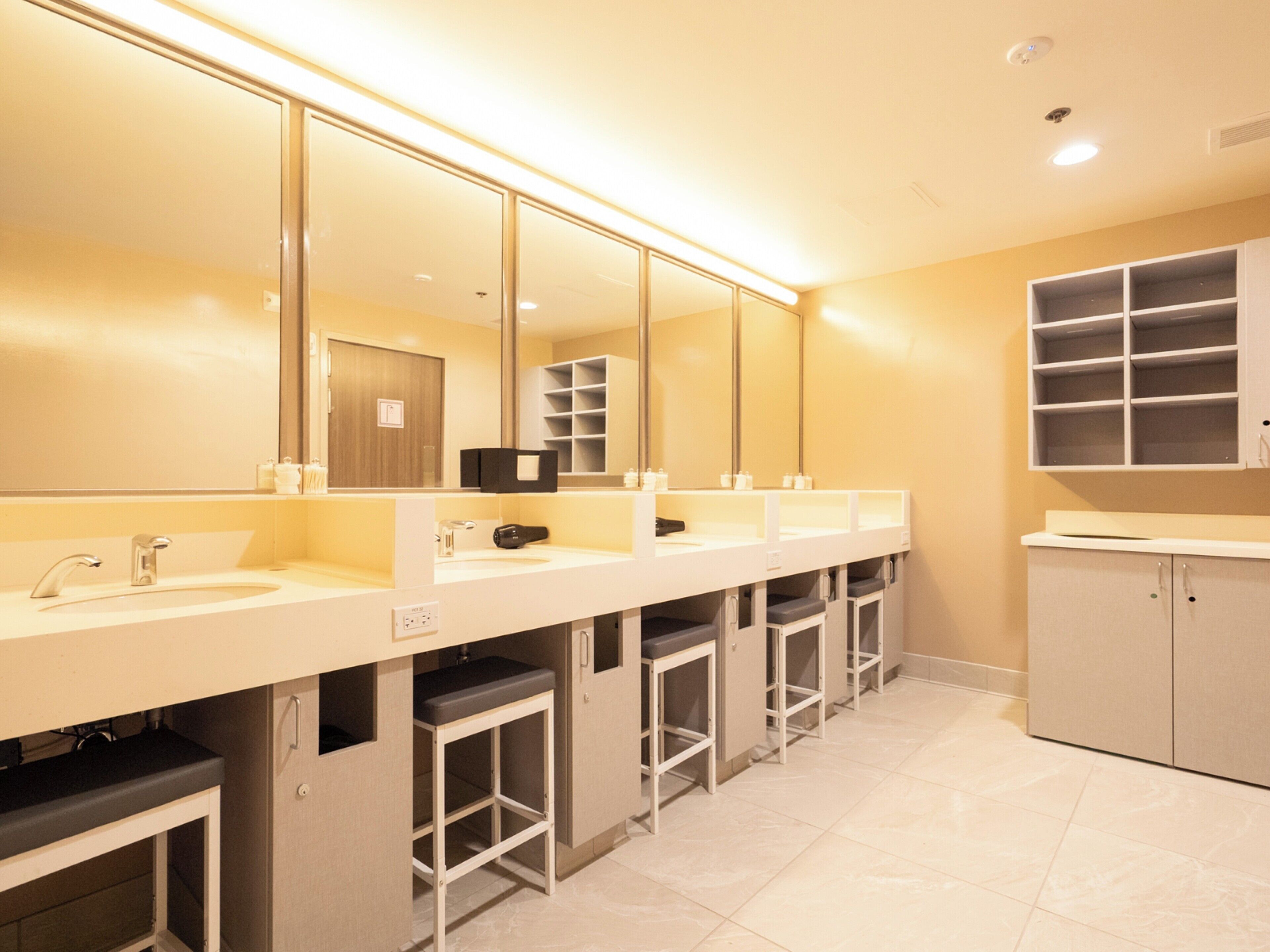 A modern bathroom with three sinks, a large mirror, and storage cabinets.