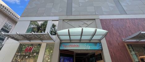 Un edificio moderno con entrada de vidrio, una tienda H&M a la izquierda y un letrero Sky Waikiki sobre la entrada.