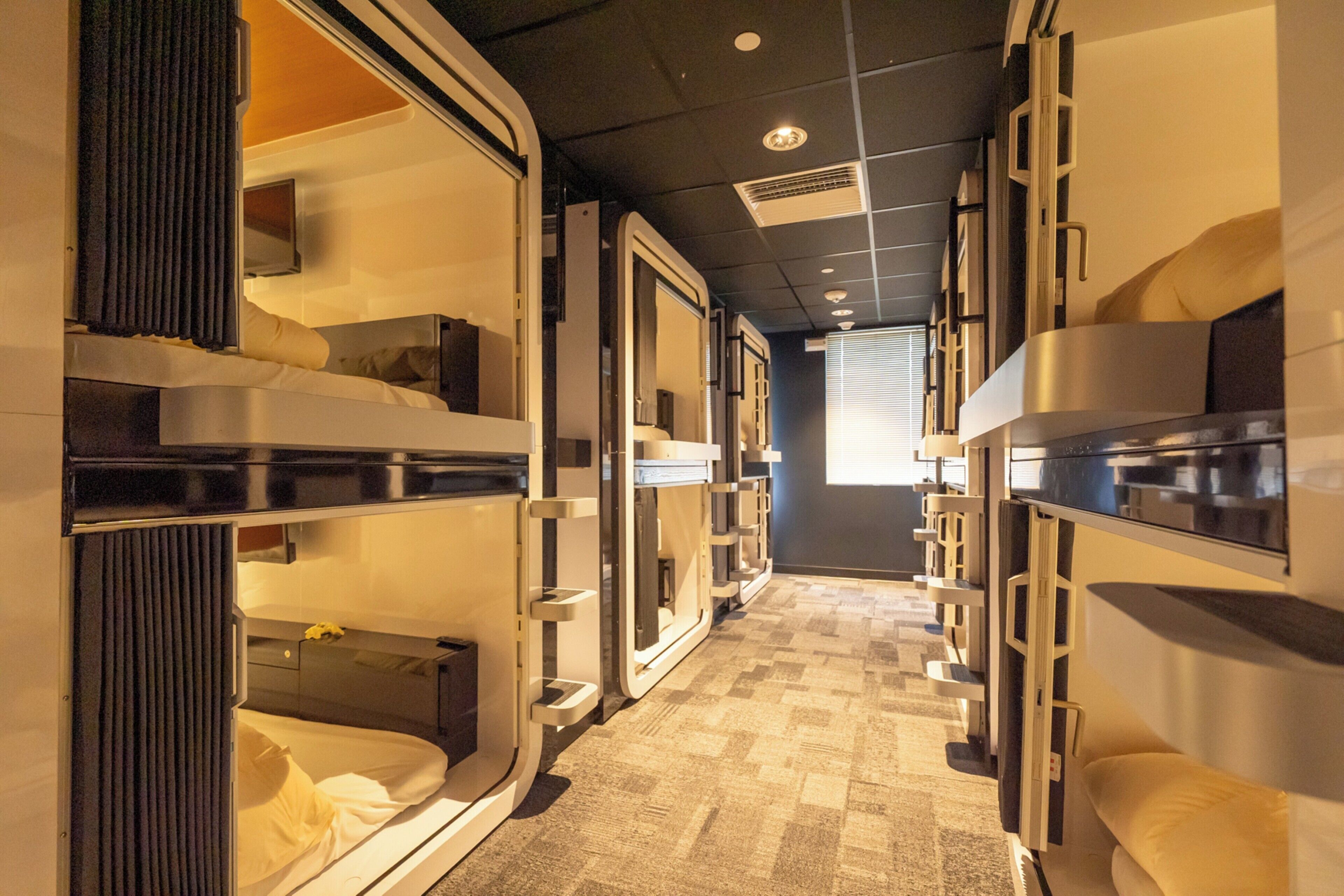 A corridor with bunk beds, a flat-screen TV, and a window with blinds.
