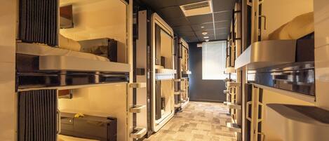 A corridor with bunk beds, a flat-screen TV, and a window with blinds.