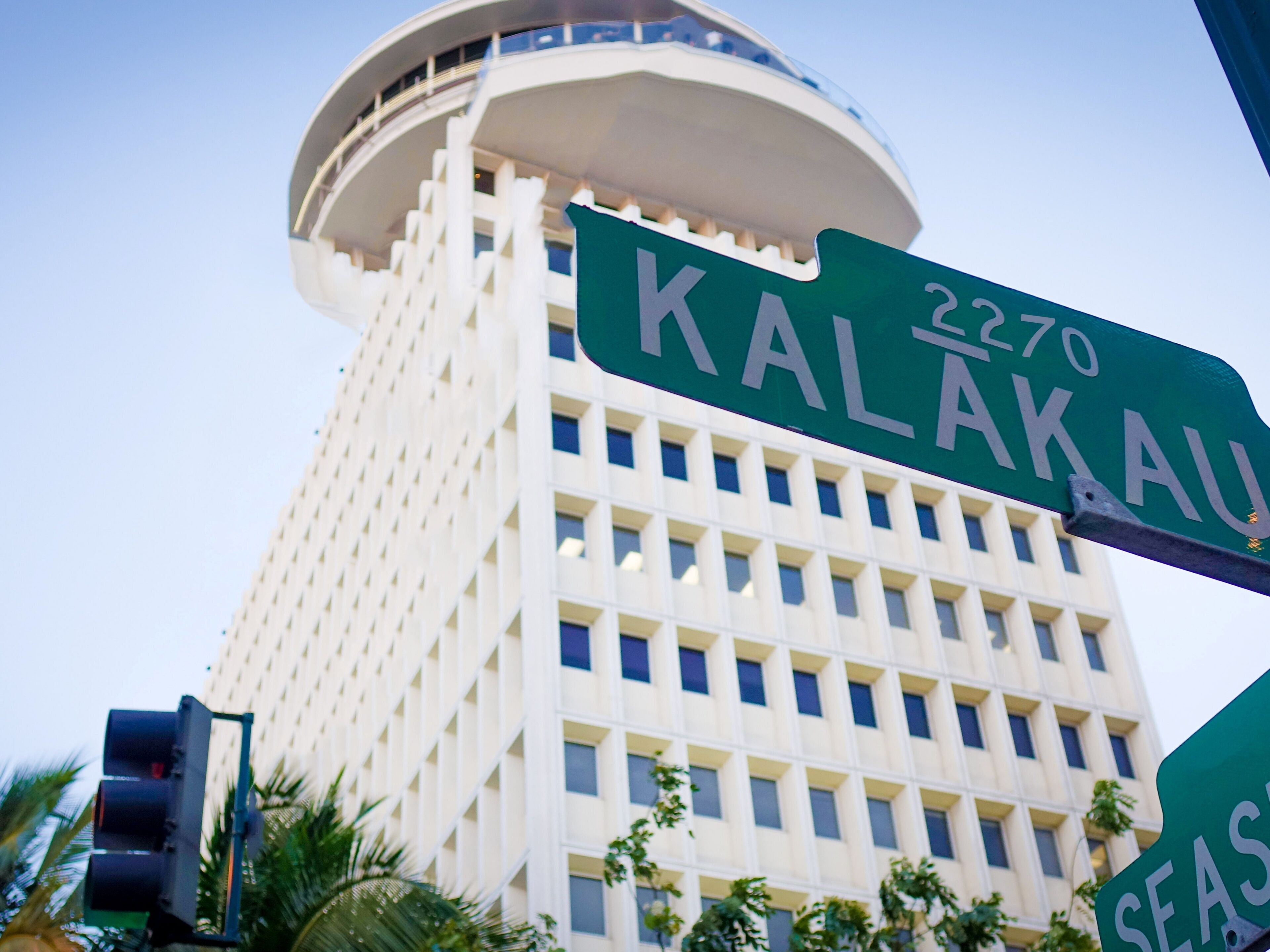 A street sign for Kalakaua Street with a modern building in the background.